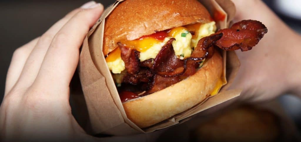 Hands holding breakfast sandwich with eggs, cheese, and bacon