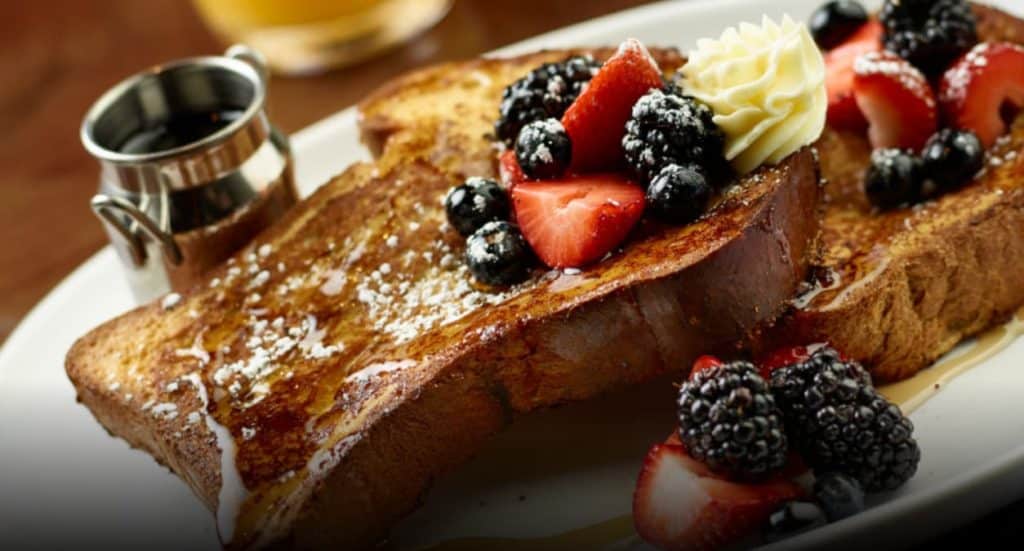 French Toast with blackberries, cut strawberries, and bluberries with powdered sugar and maple syrup