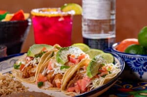 Fried fish tacos with refried beans and rice, bottle of tequila and a margarita behind them.