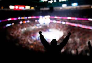 blurred image of fans surrounding a ufc fight. One person is standing with their arms raised, cheering