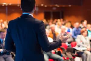 The back of a man addressing an audience at a convention center.