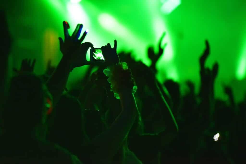 Concertgoers at a show with their arms raised. In the background are neon green lights. 