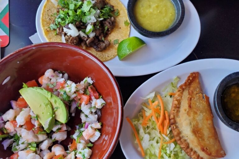 An overhead spread of Mexican dishes including shrimp ceviche, a carne asada taco, and a fried empanada, each served with salsa dipping sauces.