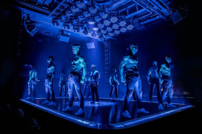 Magic Mike Live male dance troupe performing on stage under dramatic blue lights in Las Vegas.
