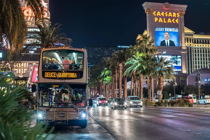Double-decker bus on the Las Vegas Strip at night, showcasing public transit options near Caesars Palace.