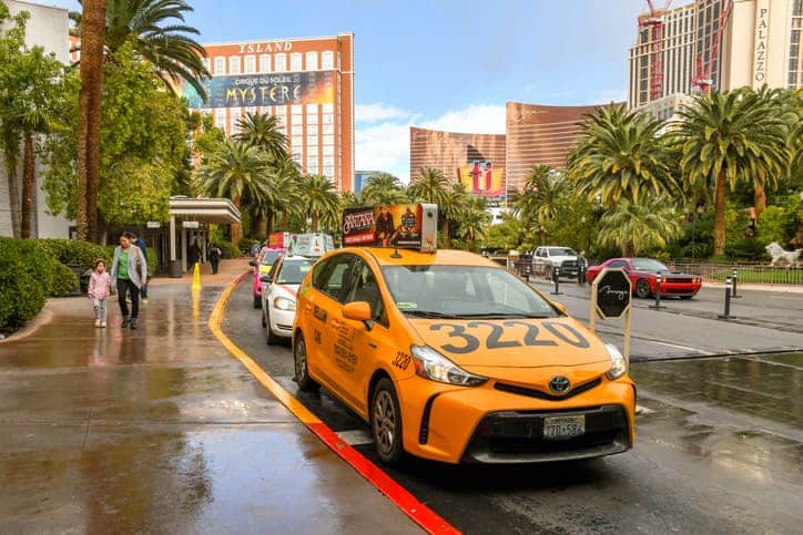 Orange taxi parked on a wet street in Las Vegas near Treasure Island, highlighting transportation options in Las Vegas.