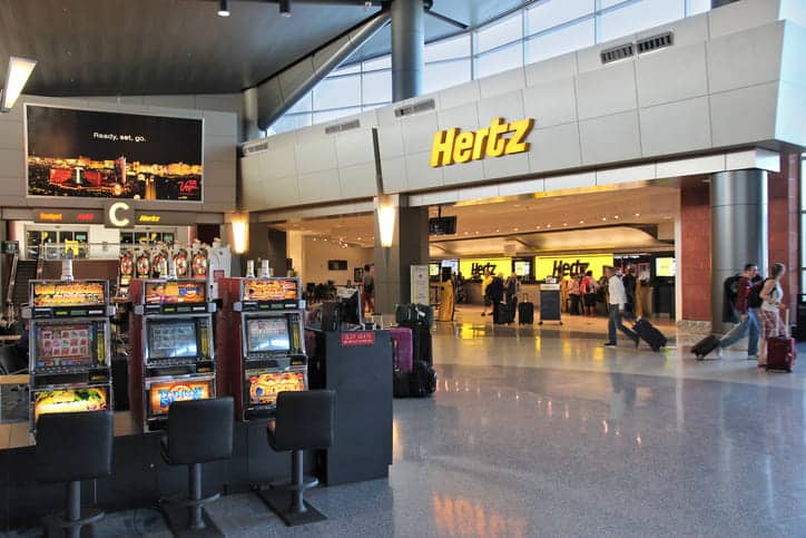 Hertz rental car center inside a Las Vegas airport, featuring slot machines and travelers, highlights vehicle rental options.