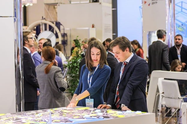World Of Concrete 2026 1 Man And Woman Discussing An Illuminated Urban Planning Layout At An Industry Conference
