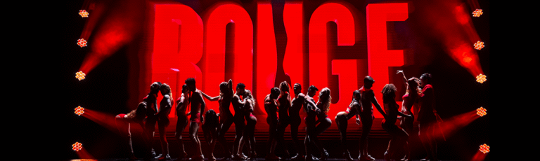 Silhouettes of dancers performing on stage in front of a bright red 'ROUGE' show logo under dramatic stage lighting.