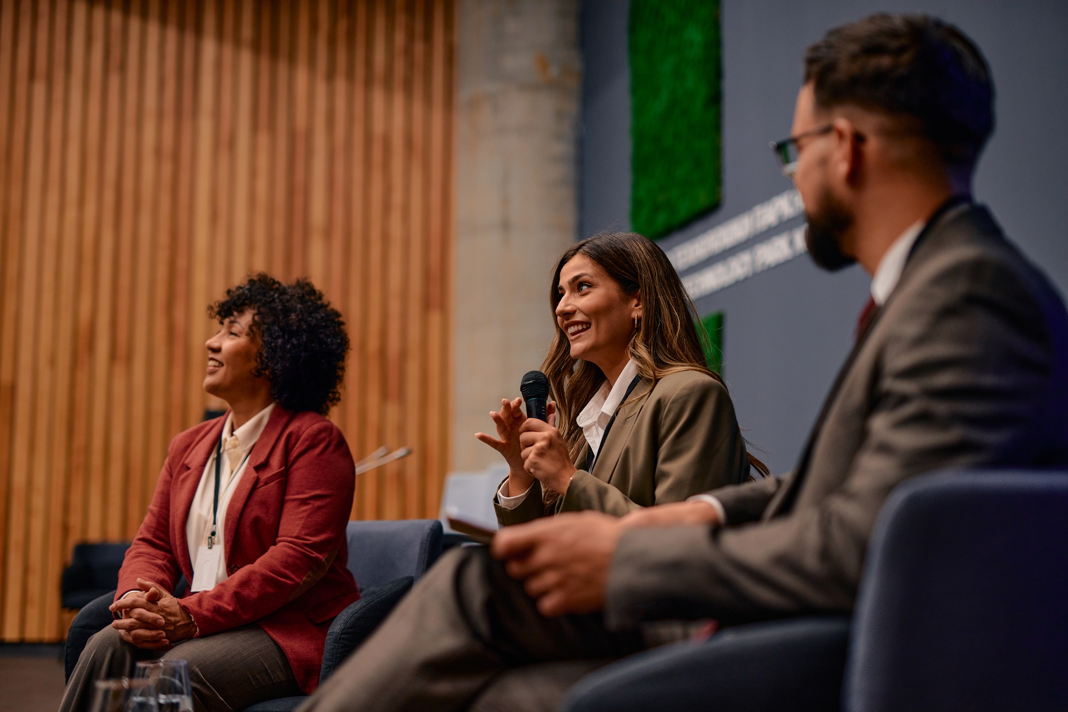 Ces Las Vegas 2026 1 Businesswoman Sitting At A Conference. Speaking Into A Microphone While Colleagues Attentively Listening To Her Insightful Presentation. Fostering Communication And Collaboration Among Professionals