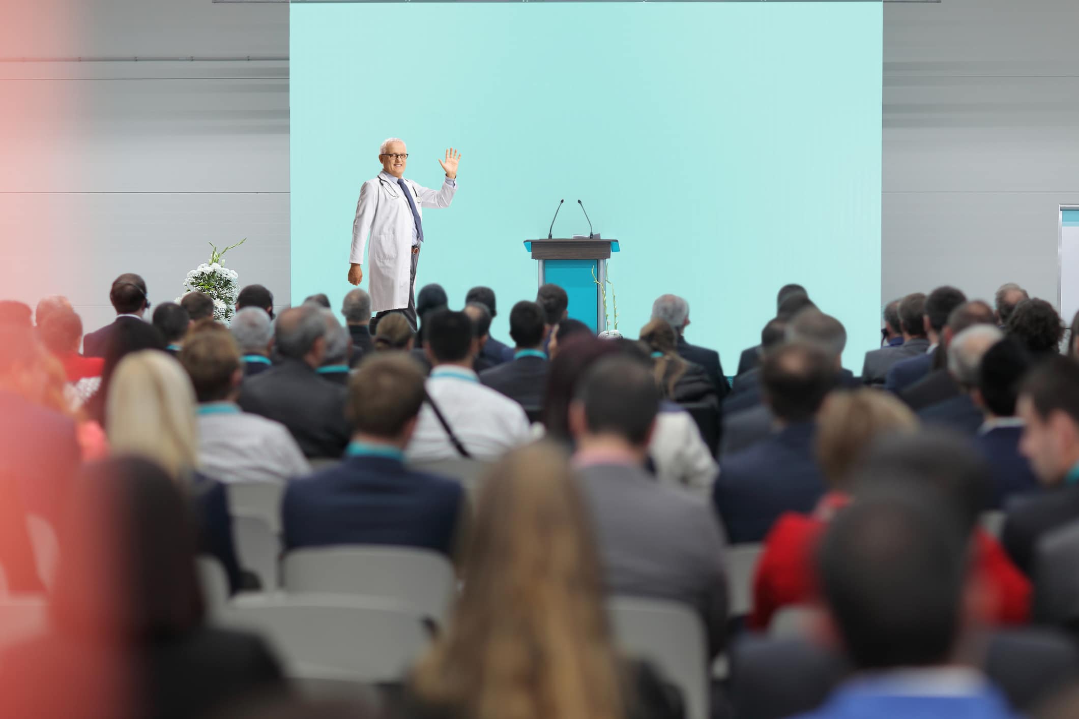 Male Doctor Waving At Audience From The Stage At A Medical Conference Event