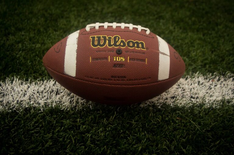 American football resting on a white yard line of a green turf grass field.
